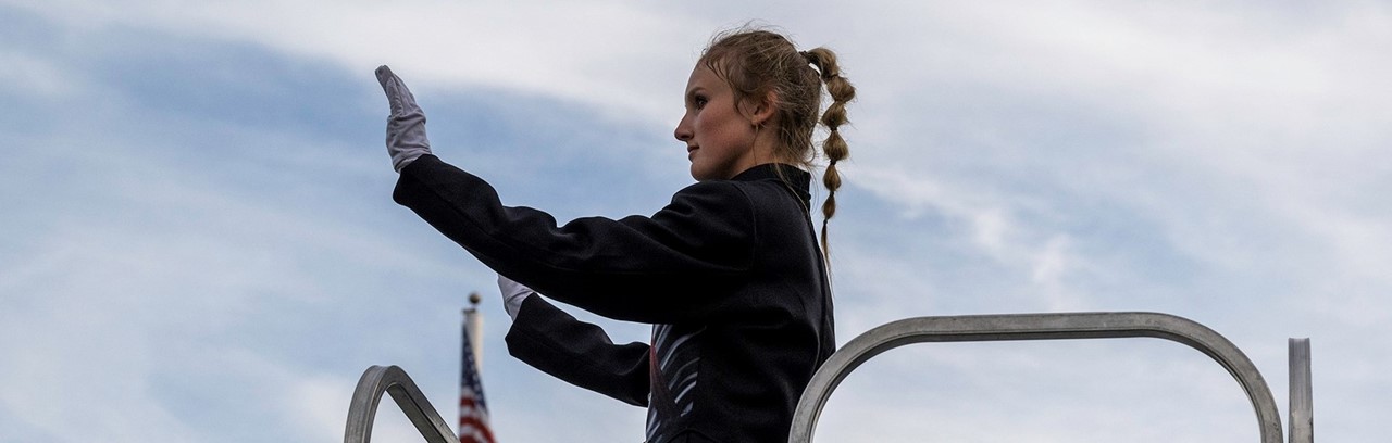young woman with a braid directing the marching band against a blue sky