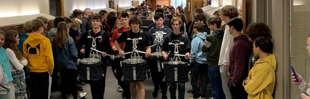 band playing in the high school hallway for a state send-off while students stand on each side