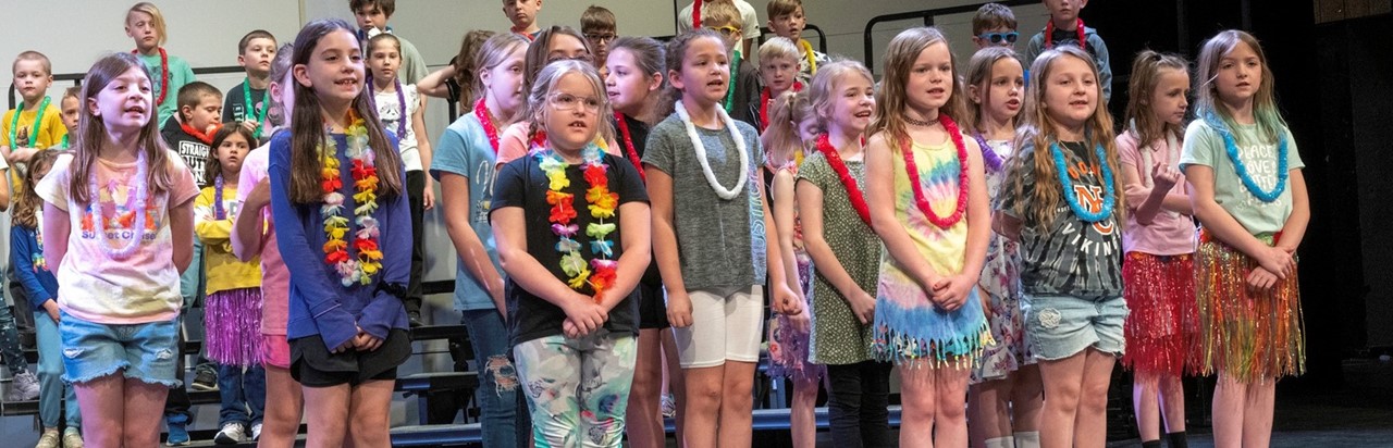 second-grade girls wearing leis and singing onstage