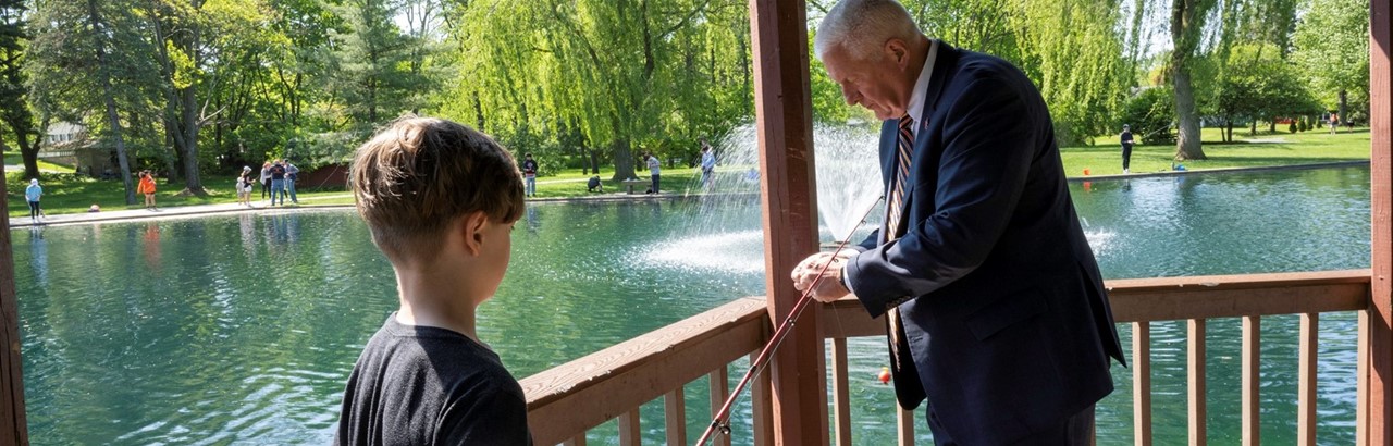 a man in a suit is baiting a young boys&#39; fishing pole