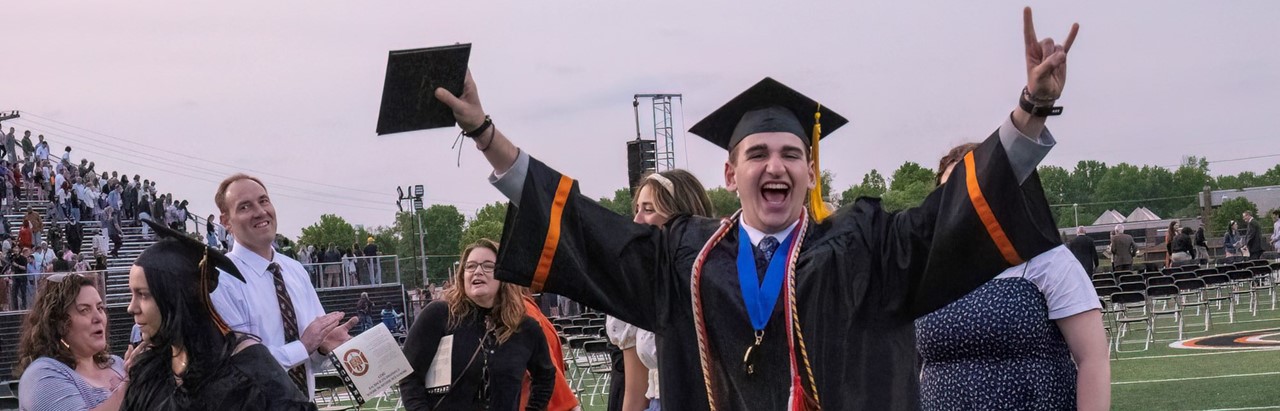 Graduate holding his arms up while carrying his diploma