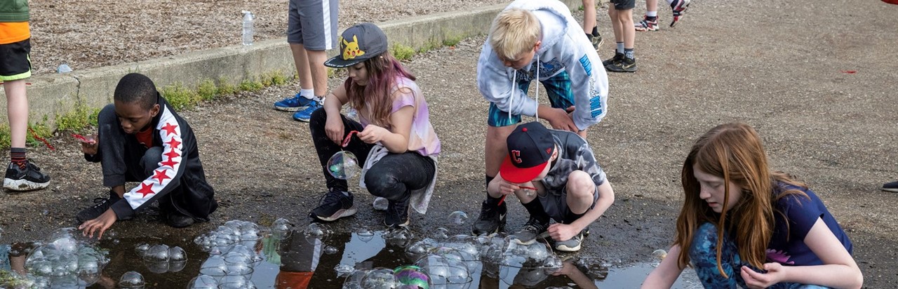 five students dipping wands in soapy water to blow bubbles
