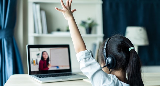 Student_Learning_Virtually_Raised_Hand Student with headphones raising hand while learning virtually on a laptop