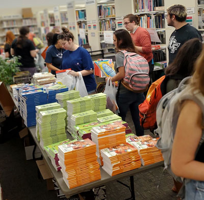 Table with stacks of books and a person looking at one