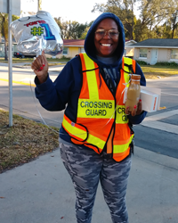 A female crossing guard holds a balloon, coffee and donut treat package