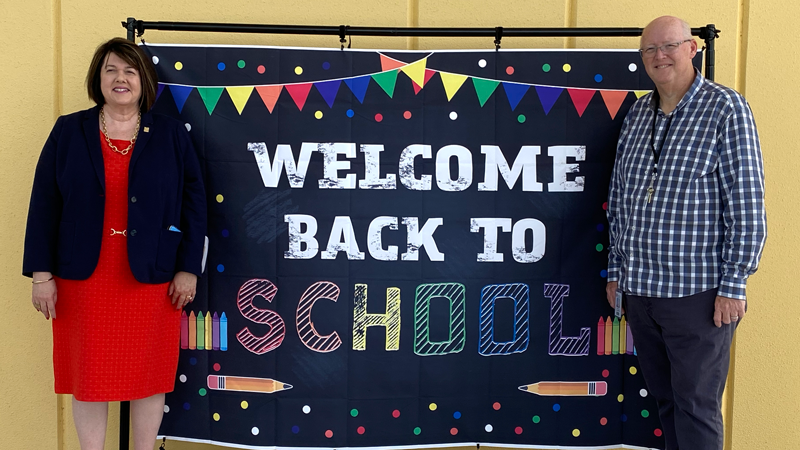 Two adults stand in front of a Welcome Back to School sign