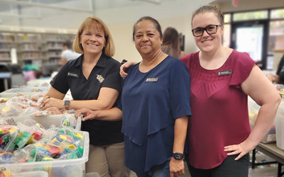 Three women pose next to a bin of manipulatives