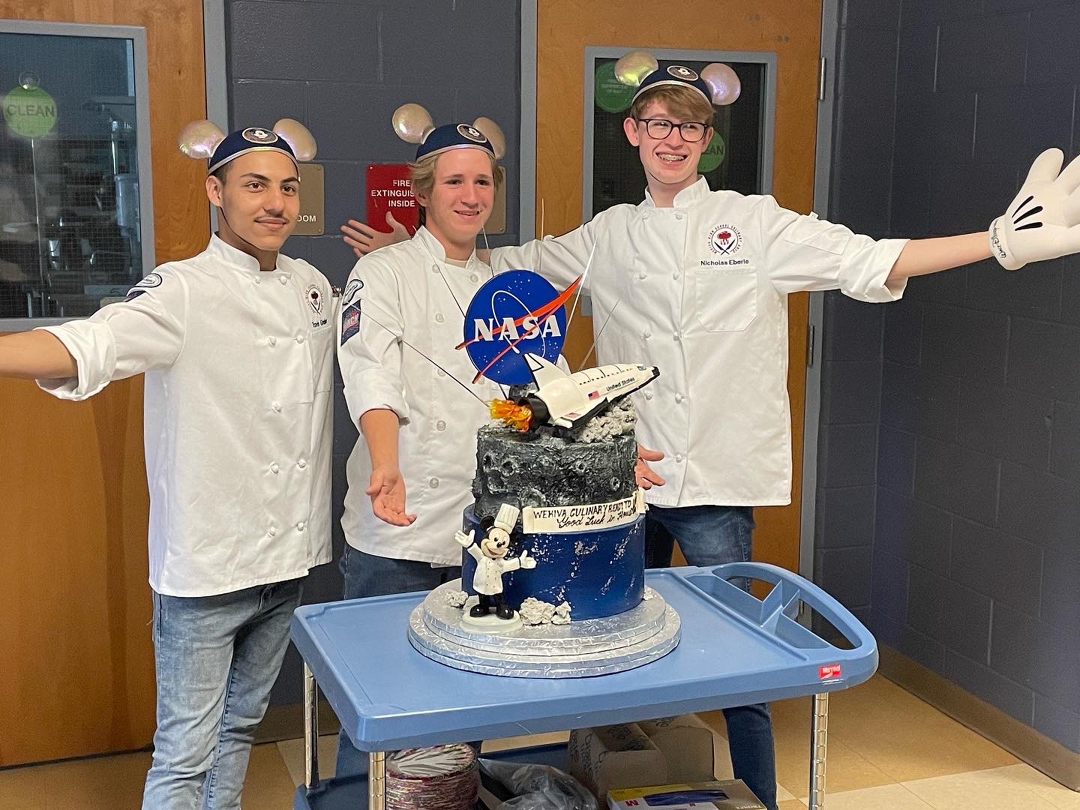 Three boys stand behind a NASA space shuttle cake