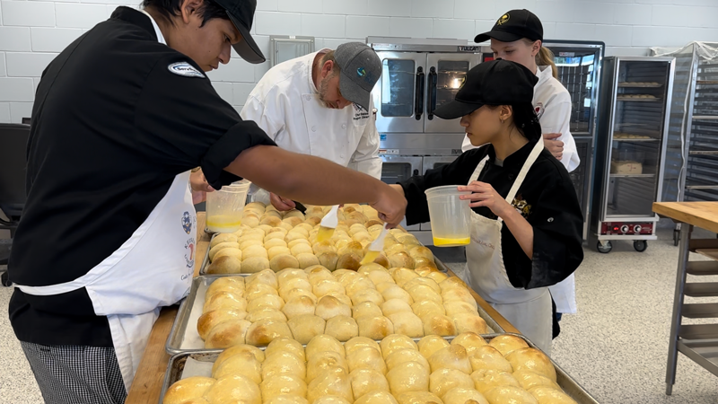 Four people butter trays of rolls