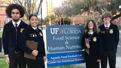 Four students smile next to a UF sign