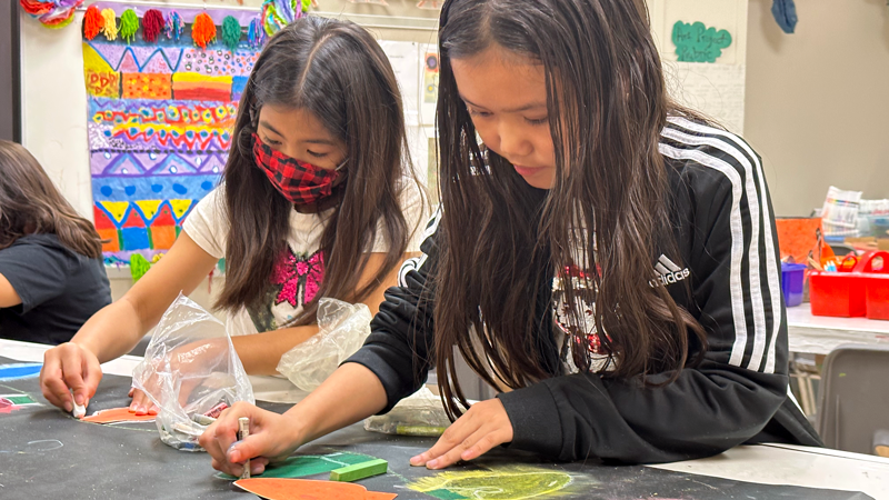 Two female students use pastel chalk to shade shapes