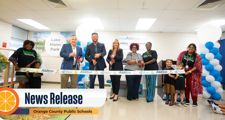 A group of people holds large scissors preparing to cut a ribbon