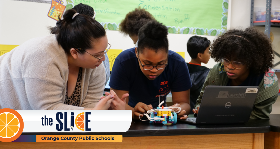 a teacher and two students look at a LEGO robot