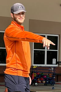 Wearing an orange sweatshirt, Sean Paino points to a student