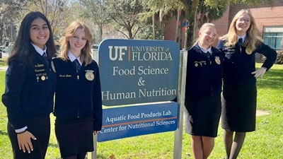 4 students pose next to a UF sign