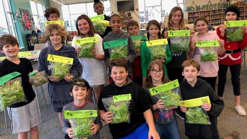 Group of students holds bags of lettuce they grew