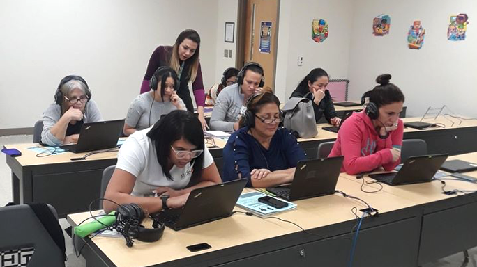 A teacher helps parents in a computer lab learn English