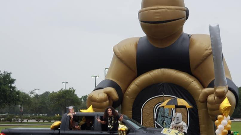 A senior female leans out a truck window in front of a blow up Knight