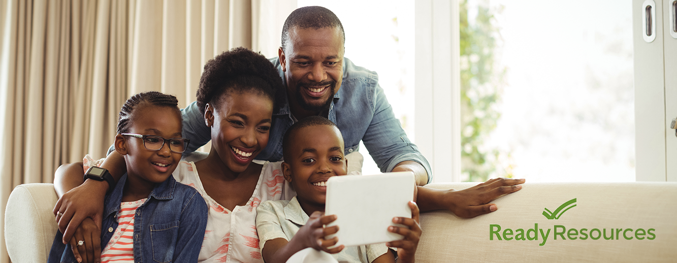 Image of a family looking at a tablet on a sofa.