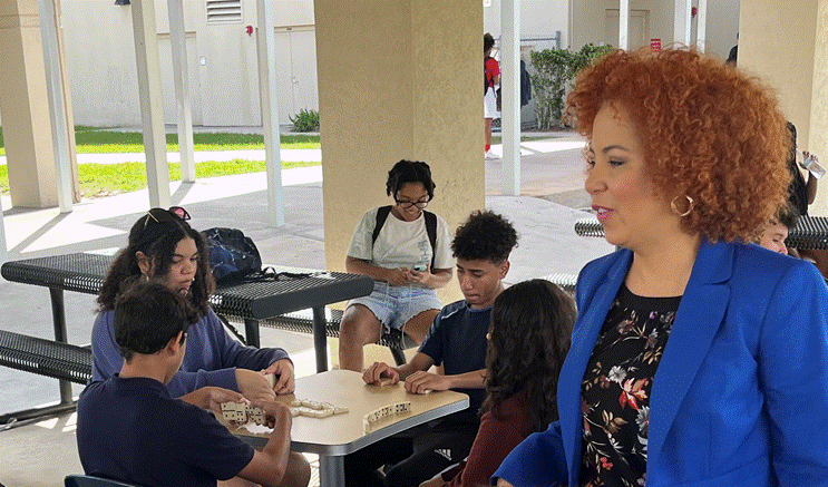 Teacher Mrs. Armenteros watching students play dominoes