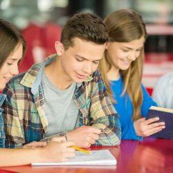 Teenage Students Sitting At Table Smiling And Reader