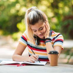 Teenage Girl With Striped Shirt Smiling While Writing In A Notebook