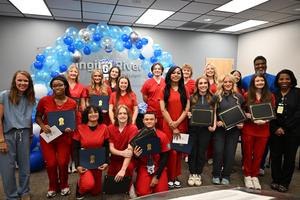 students dressed in red scrubs smile at camera next to their instructors