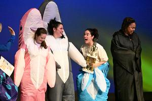 three women are dressed in shark costumes. one holds a trophy