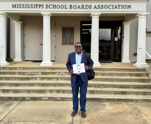 Jerry Jackson holds up his course completion certificate in front of the Mississippi School Boards Association building