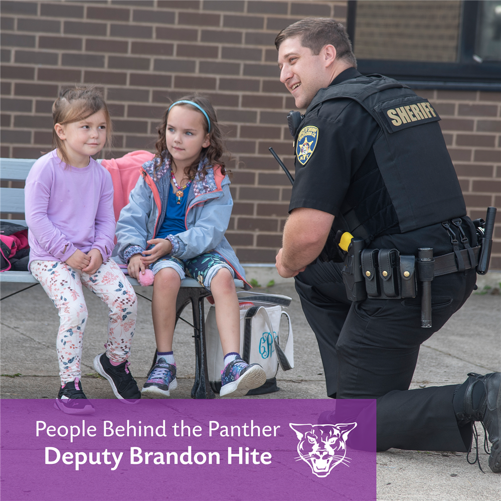 A sheriff's deputy kneels to talk to elementary students on a bench
