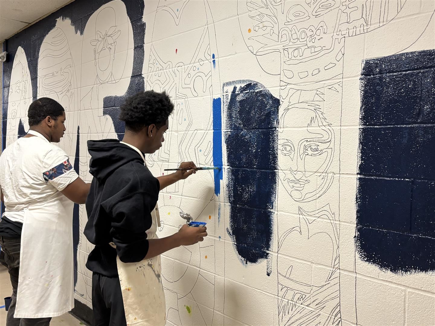 Two students paint a mural on a wall