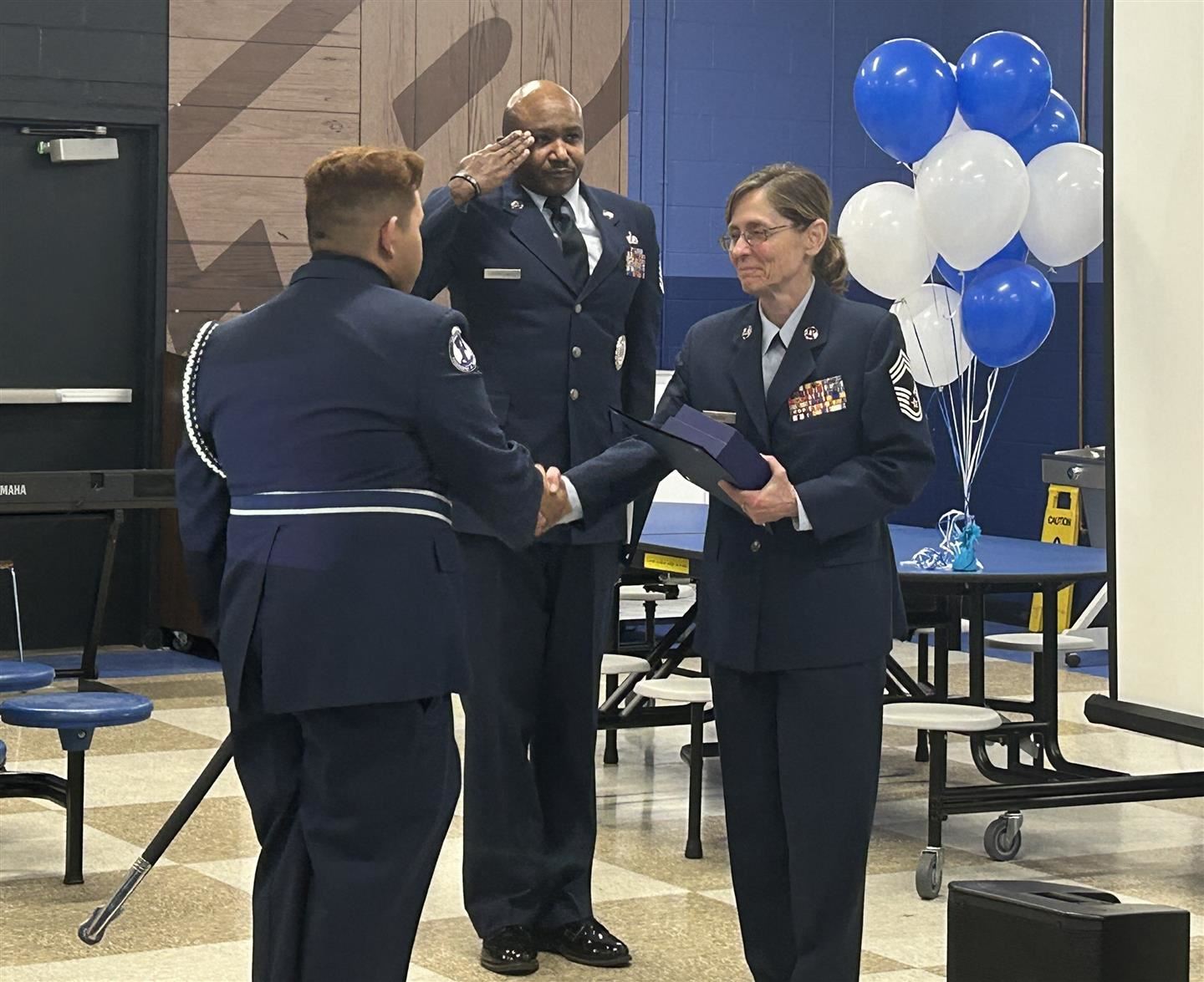 An AFJROTC instructor shakes a cadet's hand as an instructor salutes