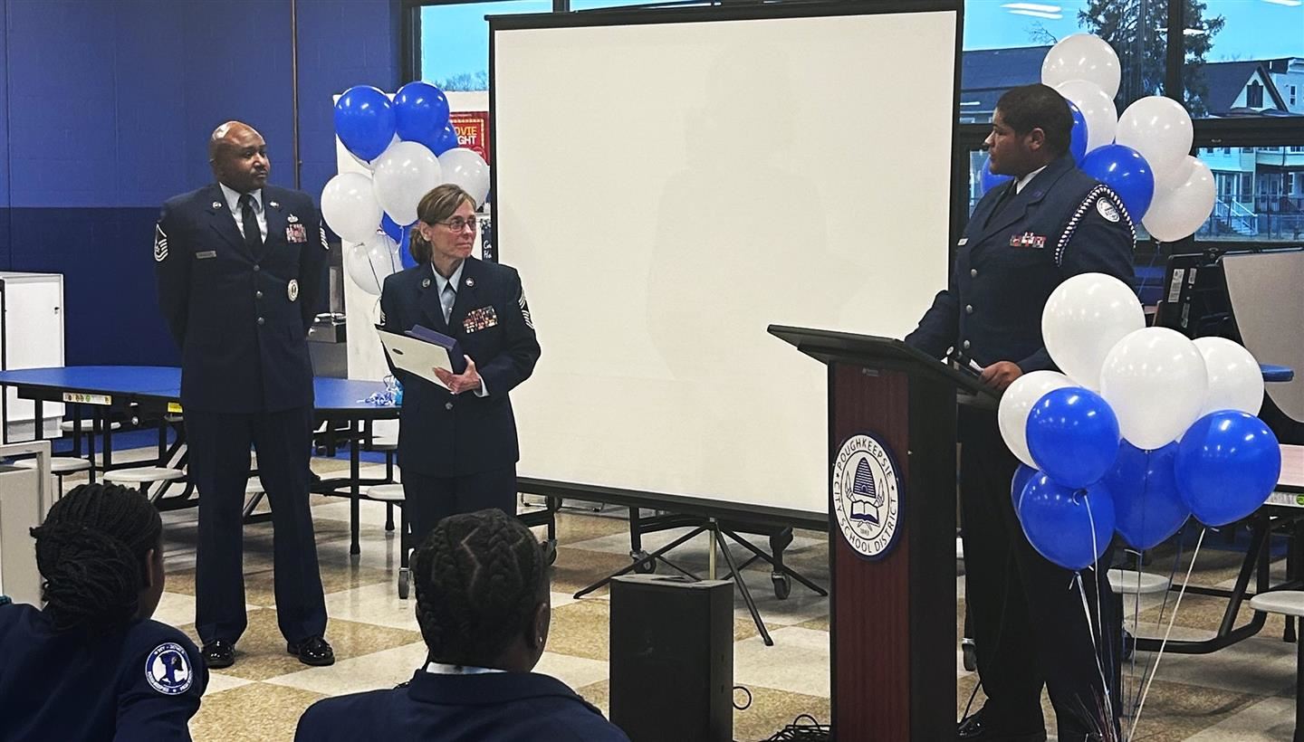  A cadet at a podium addresses two AFJROTC instructors standing off to the side