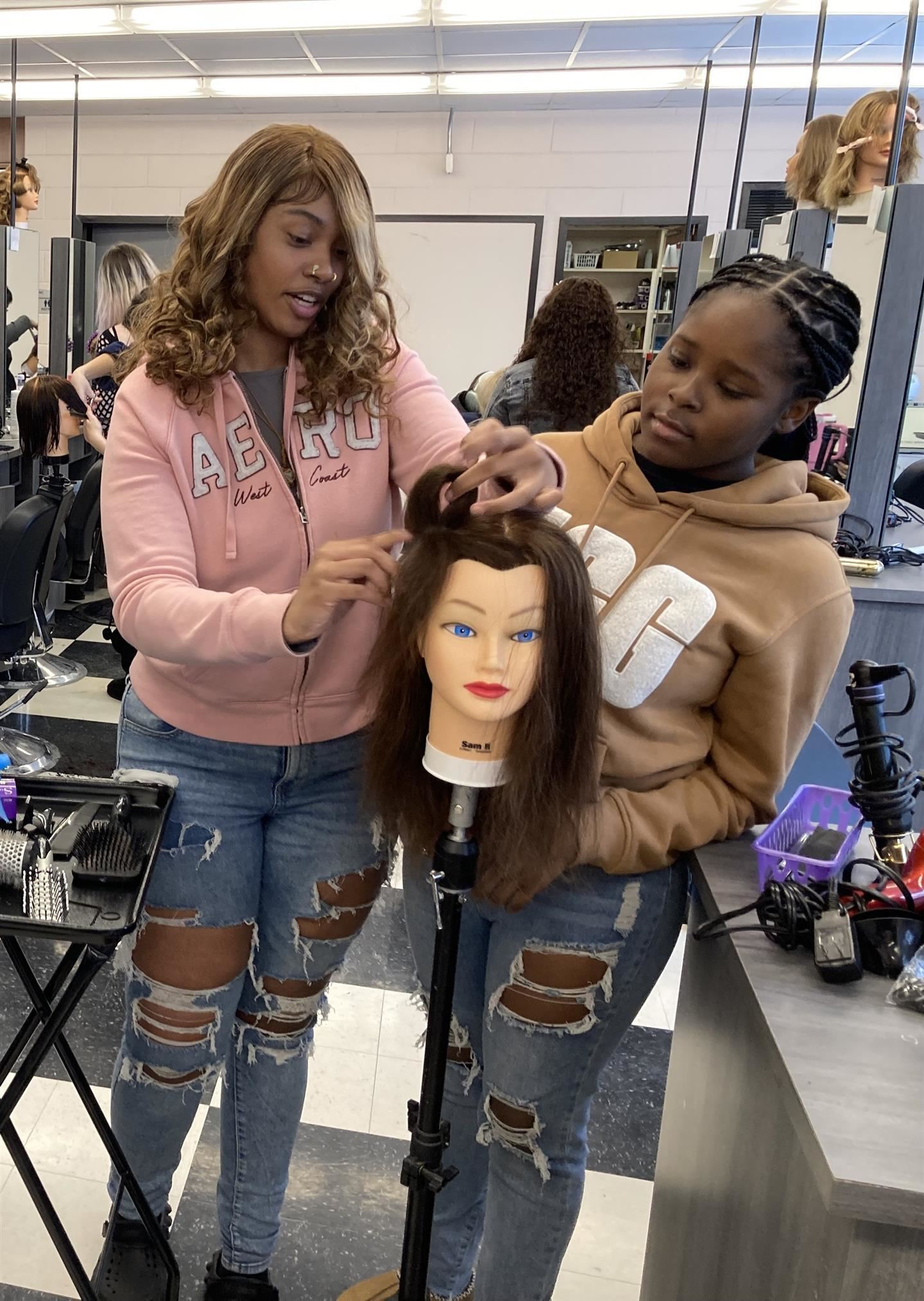 Two students style the hair of a mannequin head