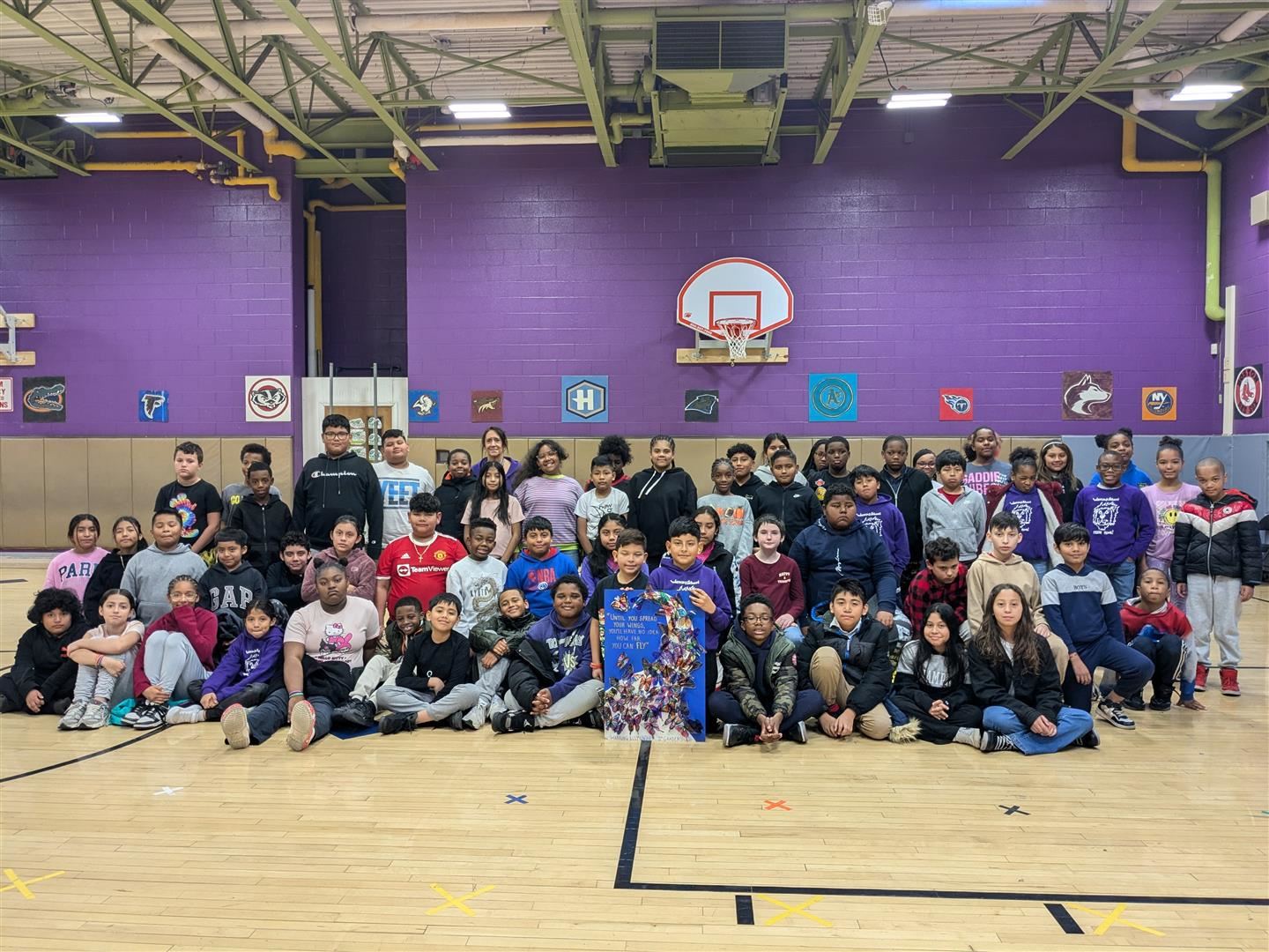 Dozens of students pose in a group with their art project