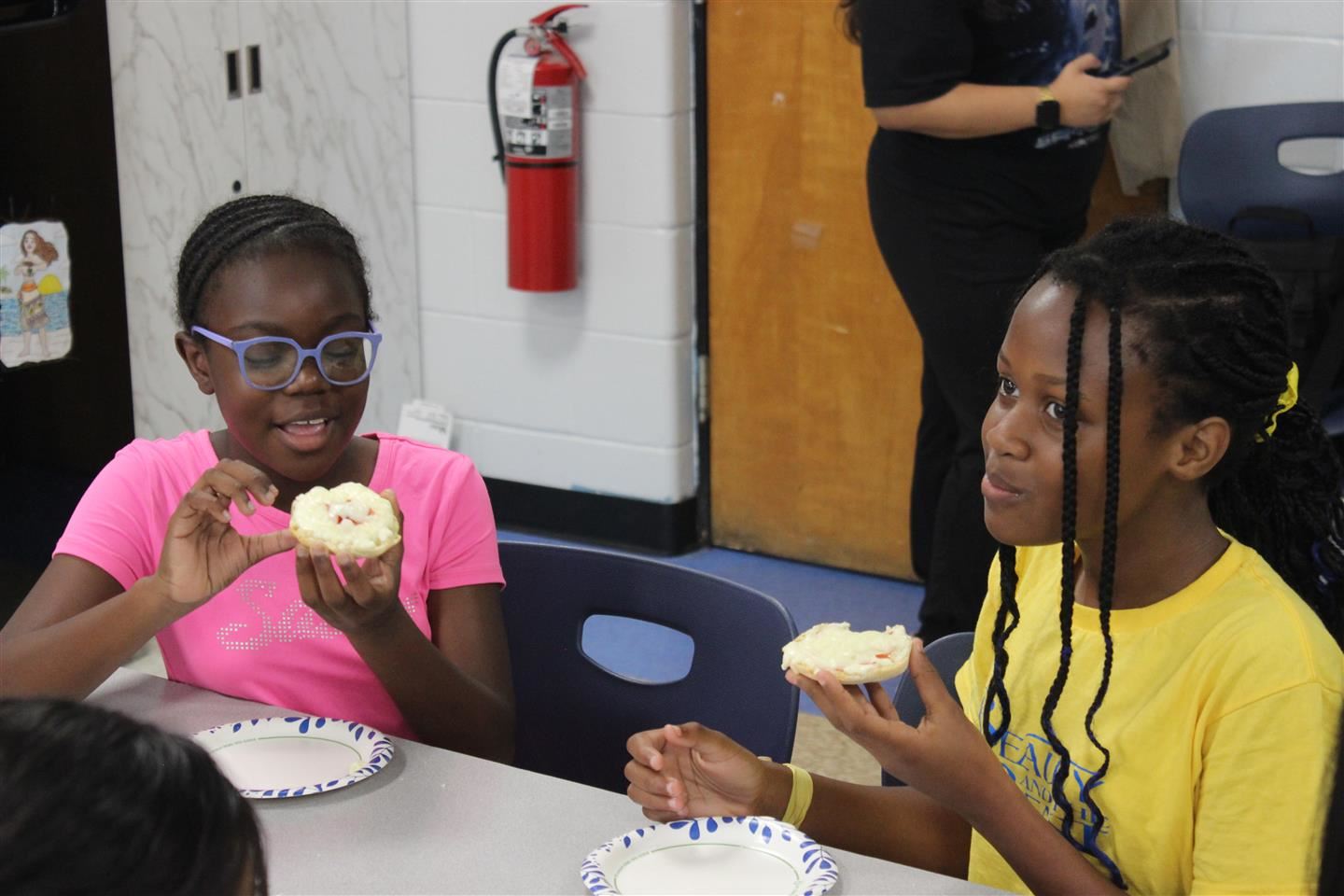 Two students eat English muffin pizzas at a table