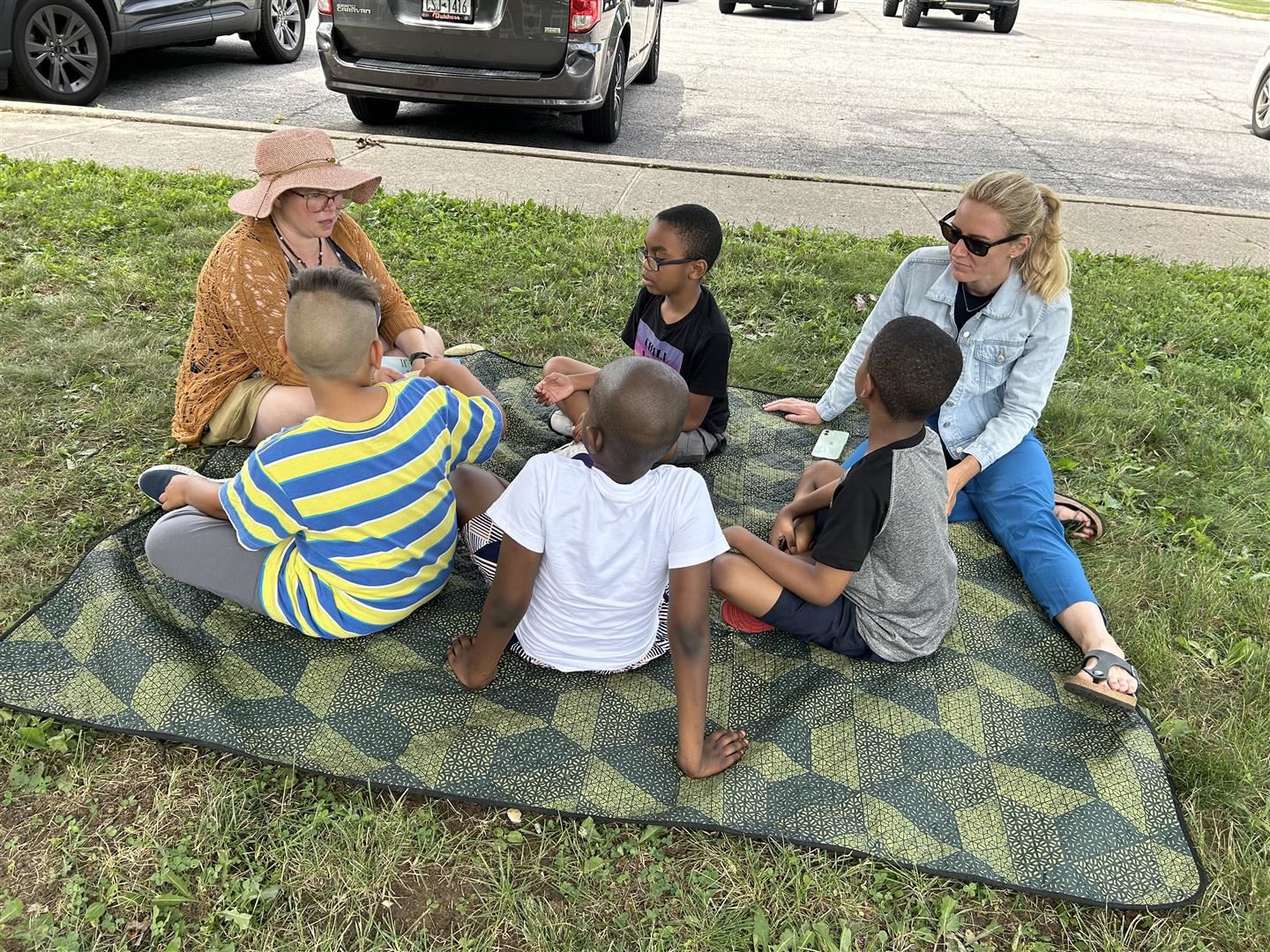 Students and teachers read on a blanket on grass