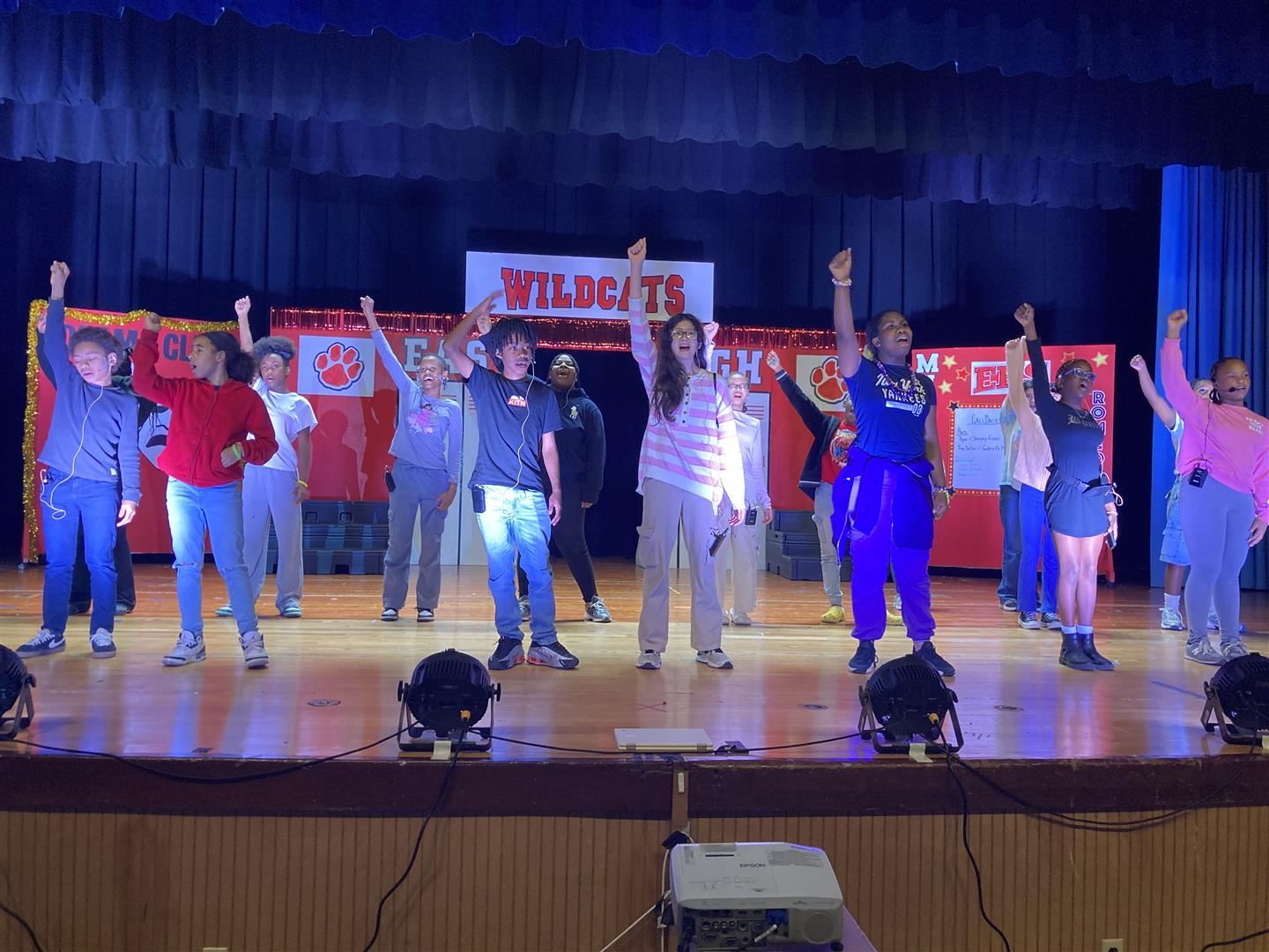  A group of students performing a play hold one hand each in the air.