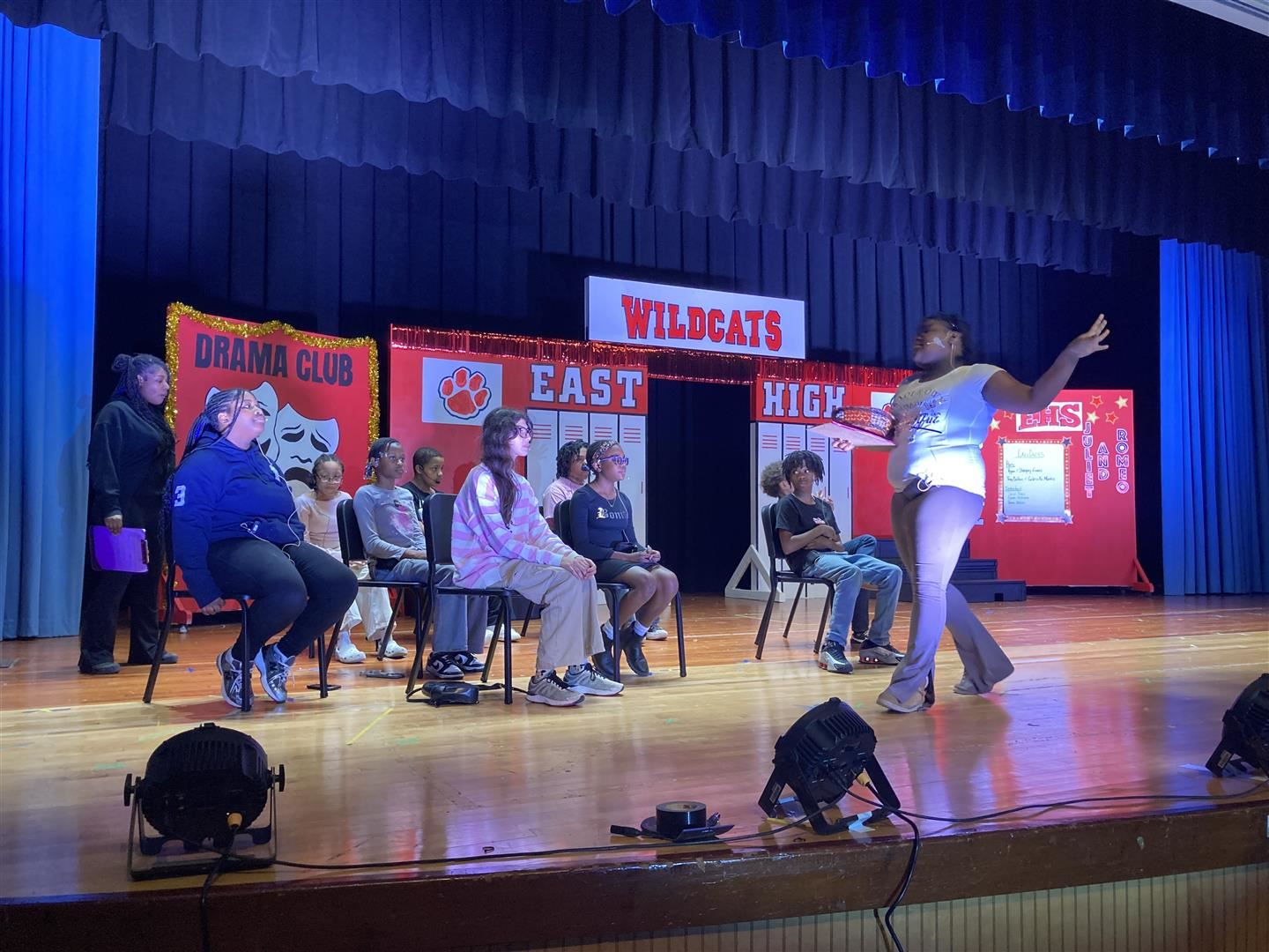 A group of students act like they're in a classroom during a play.