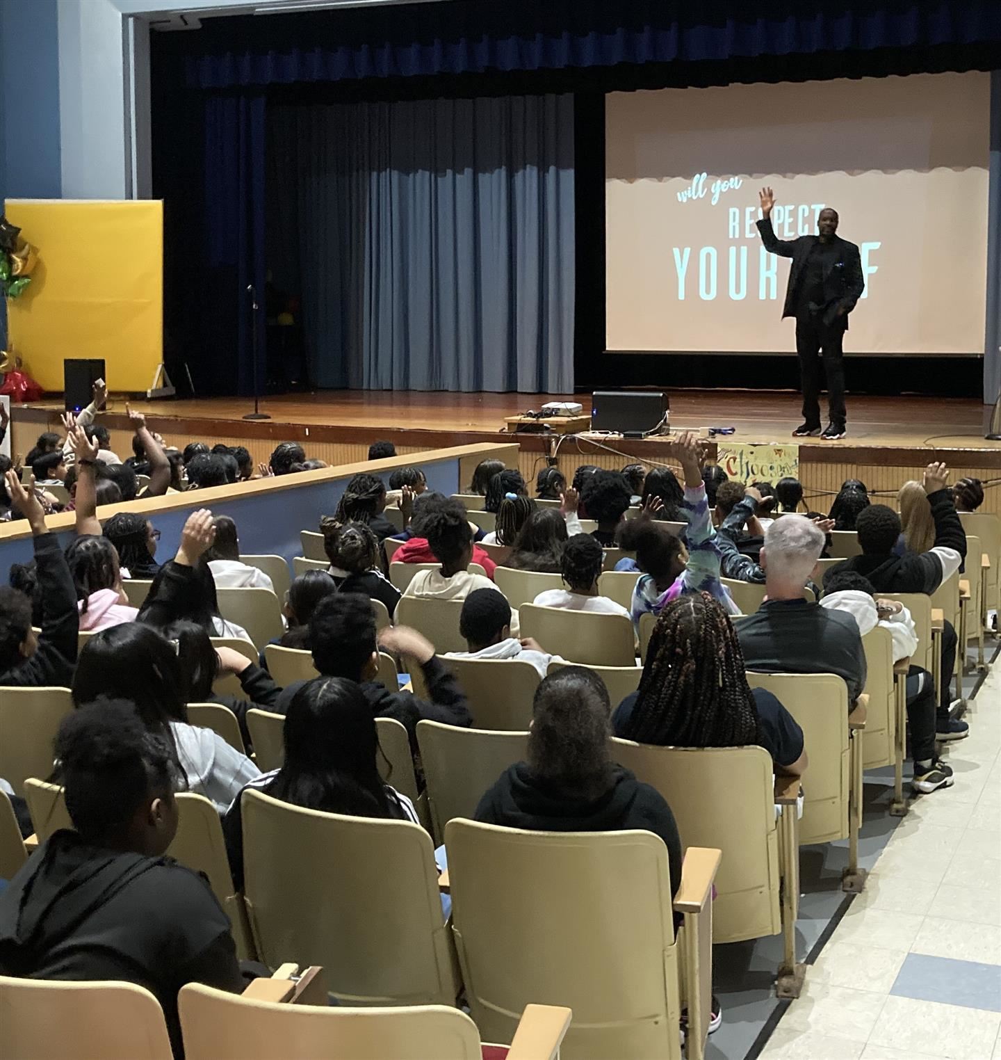 Mister Brown stands on stage and asks for a show of hands from students in the audience
