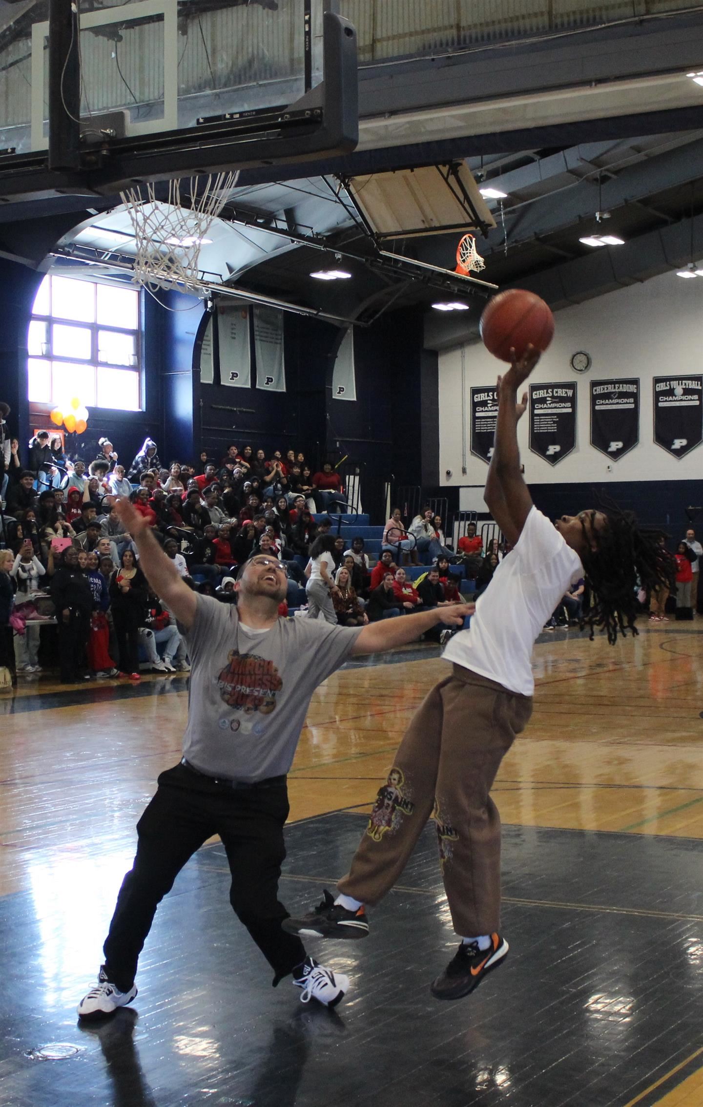 A student takes a short jump shot over a teacher.