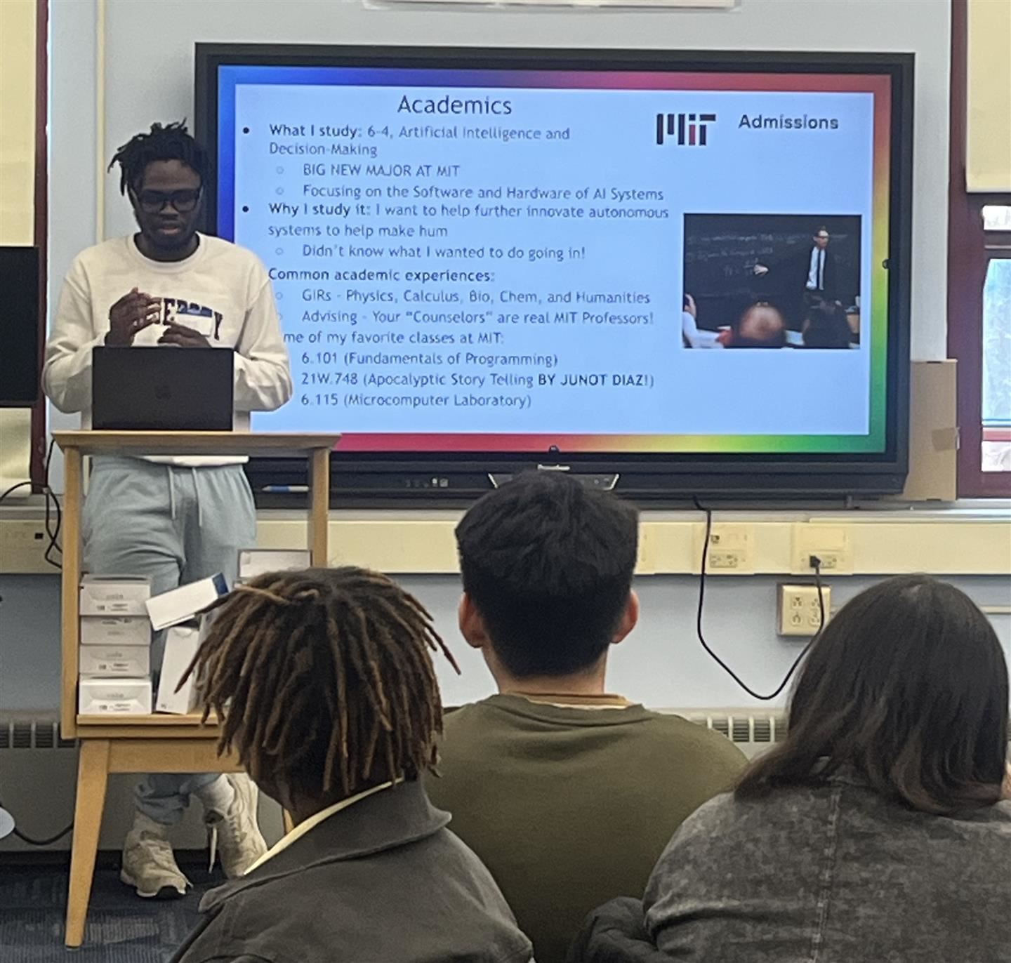 A graduate gives students a presentation with a screen behind him.
