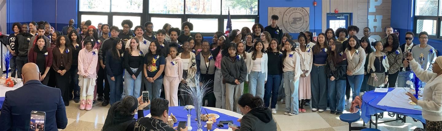 Nearly 100 students pose together in a cafeteria