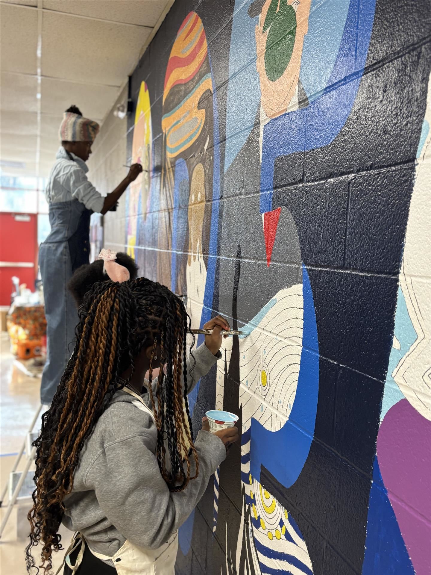 Three students paint a mural on a wall