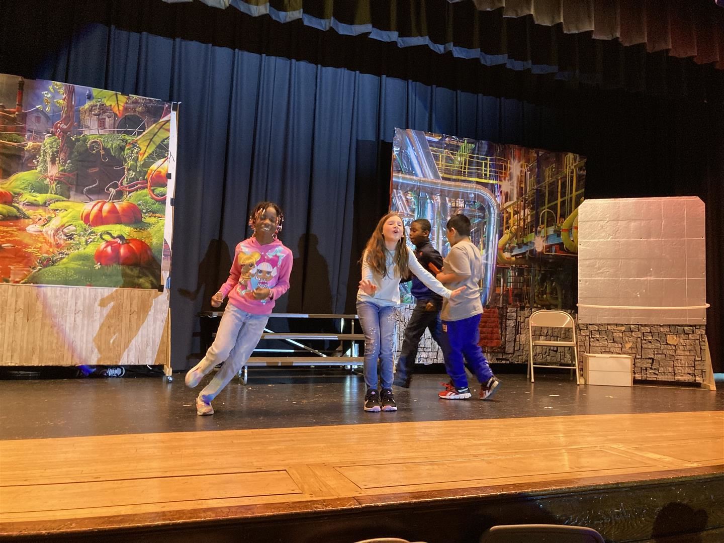 Three students run around a fourth student while rehearsing a play