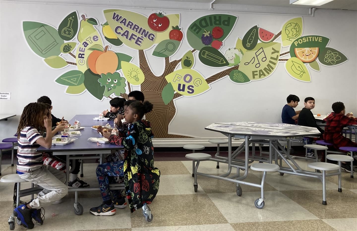  Students eat lunch in a cafeteria with a tree decal filling the wall
