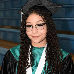 SDPA Student taking a picture in her black gown, with teal and white.