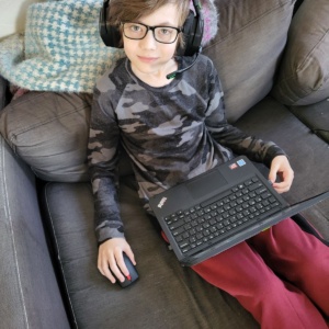 Boy sitting in his couch with a laptop. Picture consists of being the first day of school. SDPA student.
