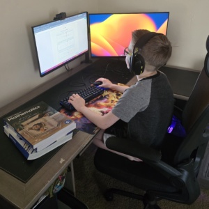 A boy sitting in his desk, working with a computer for SDPA> Picture is SDPA first day of school.