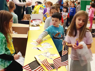 elementary students put together supplies like American flags for the troops in their classroom